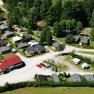 Aerial view of a campsite with caravans and small houses, surrounded by trees and meadows.