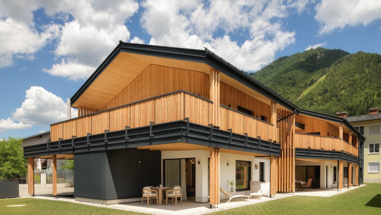 Modernes Holzgeb&auml;ude mit Balkon und Bergkulisse im Hintergrund.