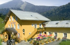 Yellow building with terrace and colorful parasols, surrounded by mountains.