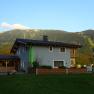 Ein modernes Haus mit grauer Fassade und Holzelementen vor einer Berglandschaft.