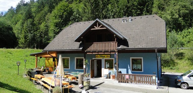 Ein blaues Geb&auml;ude mit Holzbalkon und Terrasse, umgeben von B&auml;umen.