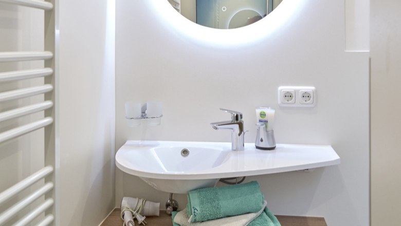 Modernes Badezimmer mit rundem Spiegel, Waschbecken und Handt&uuml;chern.