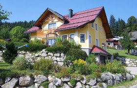 Yellow house with a red roof in a green landscape.