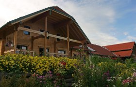 A traditional farmhouse with wooden cladding and a flowering garden in the foreground.