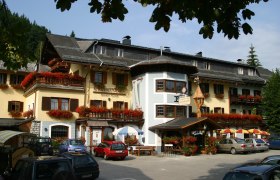 A traditional inn with flower-decorated balconies and parked cars in front of it.