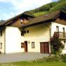 Ein zweist&ouml;ckiges Haus mit Balkon und Rosenstrauch, umgeben von gr&uuml;nen H&uuml;geln.