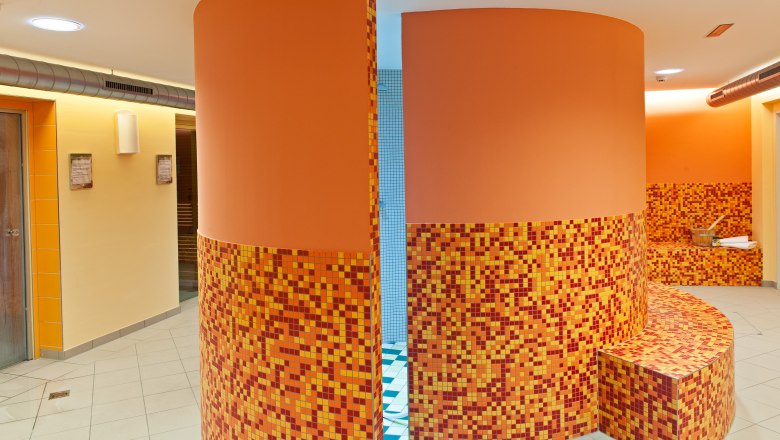 Innenansicht eines Wellnessbereichs mit orangefarbenen Mosaikfliesen und runden W&auml;nden.