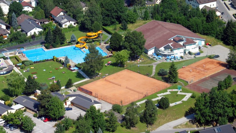 Luftaufnahme eines Freibads mit Schwimmbecken, Rutsche und Tennisplätzen in einer Wohngegend.