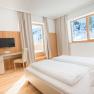 Bright hotel room with double bed, desk and view of snow-covered mountains.