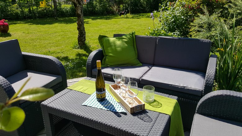 Gartenmöbel mit Weinflasche und Gläsern auf einem Tisch im Freien.