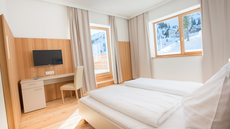 Bright hotel room with double bed, desk and view of snow-covered mountains.