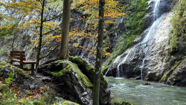 Bench by the river in the Ötscher Tormäuer Nature Park with waterfall and autumnal trees.