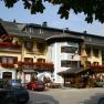 A traditional inn with flower-decorated balconies and parked cars in front of it.