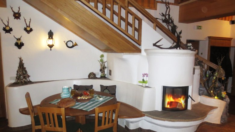 Gem&uuml;tlicher Innenraum mit Kamin, Holztisch und Treppe.