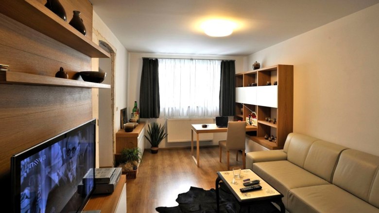 Modern furnished living room with sofa, TV, desk and shelves.