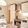 Moderne K&uuml;che mit Holz- und Wei&szlig;t&ouml;nen, Esstisch, H&auml;ngelampe und K&uuml;chenger&auml;ten.