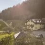Ein Bauernhof in einer l&auml;ndlichen Umgebung mit gr&uuml;nen Wiesen und einem Wald im Hintergrund.