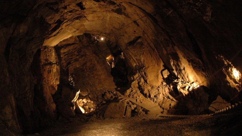 Innenansicht einer beleuchteten H&ouml;hle mit steinigen W&auml;nden und einem schmalen Pfad.