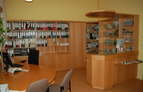 Innenansicht eines B&uuml;ros mit Holzregalen, Aktenordnern und einem Empfangstresen.