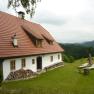 Ein traditionelles Ferienhaus mit rotem Ziegeldach in einer grünen, hügeligen Landschaft.