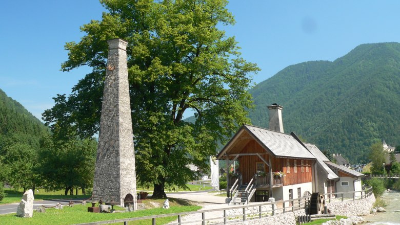 Historisches Gebäude mit Schornstein und Wasserrad in ländlicher Umgebung.