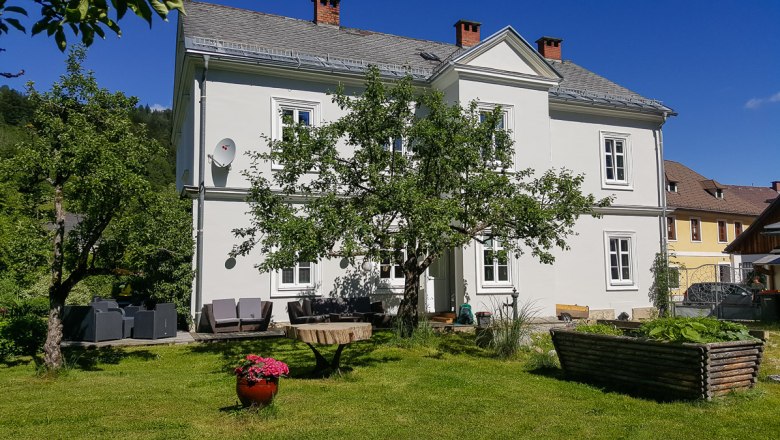 Ein weißes zweistöckiges Haus mit Garten und Bäumen.