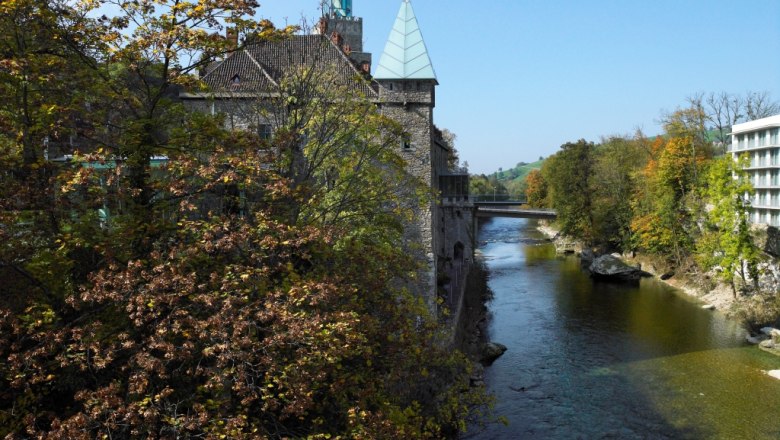 Fluss mit Herbstbäumen und Gebäude im Hintergrund.