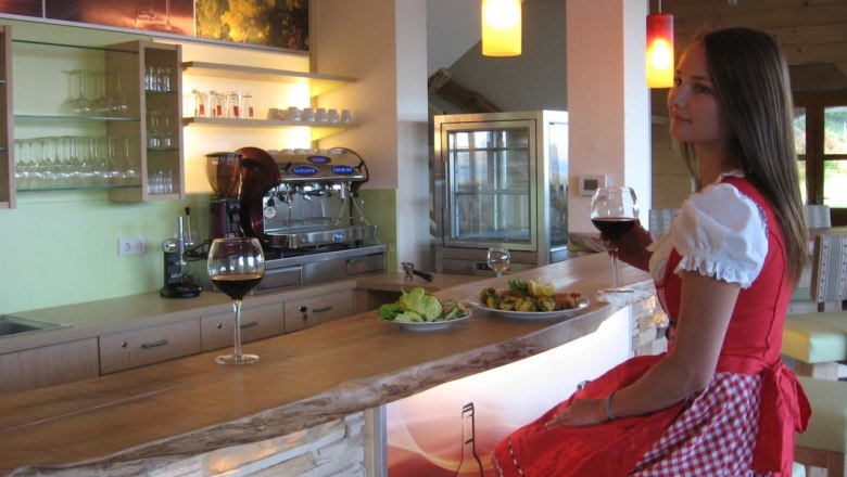 Frau in traditioneller Kleidung sitzt an einer Bar mit einem Glas Rotwein.