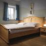 Ein Schlafzimmer mit einem Holzbett, Nachttisch und Lampe, blauen Vorh&auml;ngen und einem Bild an der Wand.