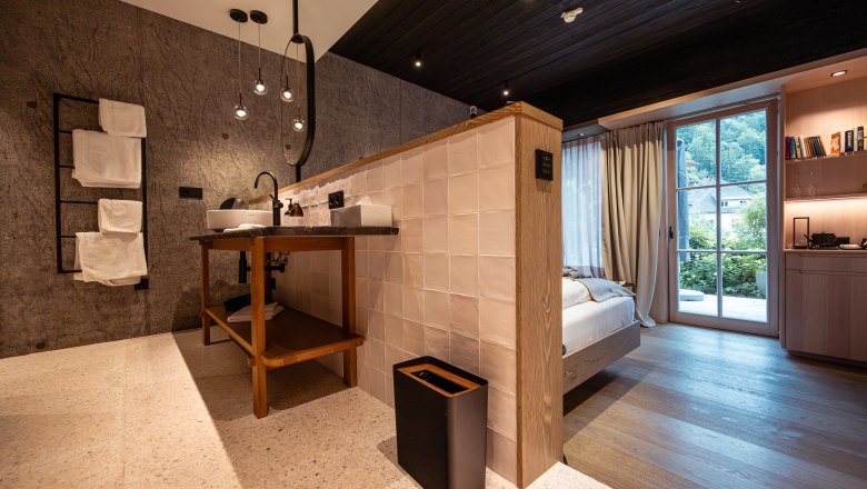 Modernes Hotelzimmer mit offenem Badezimmer, Holzboden und großen Fenstern mit Blick ins Grüne.