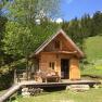 Eine kleine Holzhütte in einer grünen, bewaldeten Landschaft mit blauem Himmel.