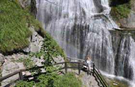 Eine Frau steht auf einer Treppe vor einem Wasserfall in der Wasserlochklamm Palfau.