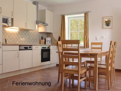 Helle Küche mit Esstisch und Stühlen, Fenster mit Vorhängen, Fliesenboden.