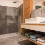 Modernes Badezimmer mit grauen Fliesen, einer Glasdusche und einem Holzwaschtisch mit Handt&uuml;chern.
