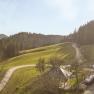 Panorama eines Bauernhofs in einer h&uuml;geligen Landschaft mit Wald und Bergen im Hintergrund.