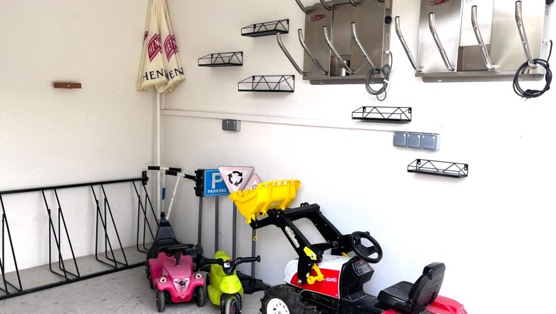 Innenansicht einer Garage mit Kinderfahrzeugen und Skischuhhaltern an der Wand.