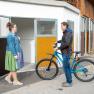 Eine Frau in traditioneller Kleidung steht vor einem offenen Schiraum, w&auml;hrend ein Mann mit einem Fahrrad daneben steht.