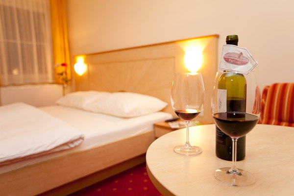 A cozy hotel room with a double bed, two wine glasses and a bottle of wine on a table.