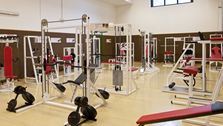 Fitnessstudio mit verschiedenen Trainingsgeräten und roten Polstern.