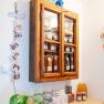 Ein rustikaler Holzschrank mit Glast&uuml;ren, gef&uuml;llt mit selbstgemachten Produkten wie Marmeladen und S&auml;ften. Darunter stehen weitere Gl&auml;ser und Flaschen auf einem Regal.