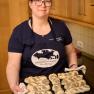 Eine Frau in einer K&uuml;che h&auml;lt ein Blech mit frisch gebackenen Mohnbr&ouml;tchen.