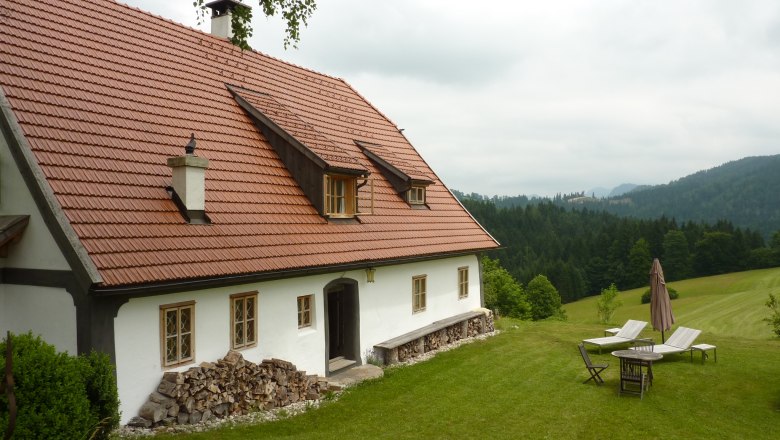 Ein traditionelles Ferienhaus mit rotem Ziegeldach in einer grünen, hügeligen Landschaft.
