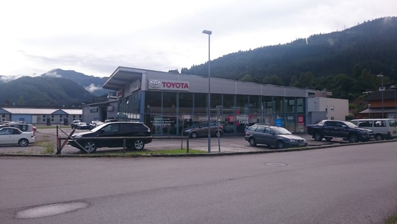 Autohaus Rottner mit Toyota-Logo und mehreren geparkten Autos vor einem Gebäude in einer bergigen Landschaft.