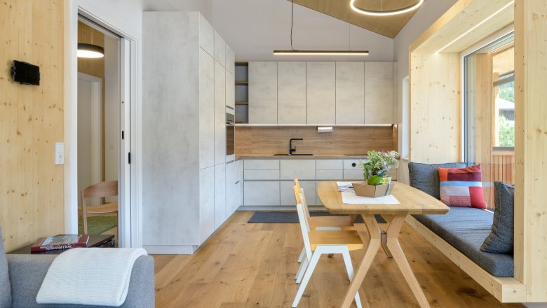 Moderne K&uuml;che mit Holz- und Betonoptik, Esstisch und Sitzbank am Fenster.