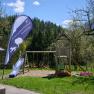Spielplatz mit Rutsche und Schaukeln, umgeben von B&auml;umen und Natur.
