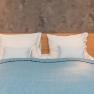 Ein Doppelbett mit blauer Decke und weißen Kissen vor einer grauen Wand.