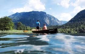 Two people in a boat on a lake, surrounded by mountains and trees.