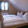 Gem&uuml;tliches Schlafzimmer mit Holzw&auml;nden, einem Doppelbett und einem Fenster mit blau karierten Vorh&auml;ngen.