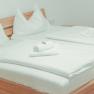 Ein gem&uuml;tliches Doppelbett in einem hellen Zimmer mit Holzrahmen und wei&szlig;en Bettlaken, dekoriert mit gefalteten Handt&uuml;chern.