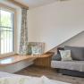 Wohnzimmer mit gro&szlig;em Fenster, grauem Sofa und Holzboden.